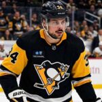 Toronto Maple Leafs captain Auston Matthews in a Pittsburgh Penguins black and gold jersey, and number 34, with a modern Highmark patch, looking towards the ice during an NHL game. Blurred arena crowd in background.