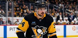 Toronto Maple Leafs captain Auston Matthews in a Pittsburgh Penguins black and gold jersey, and number 34, with a modern Highmark patch, looking towards the ice during an NHL game. Blurred arena crowd in background.
