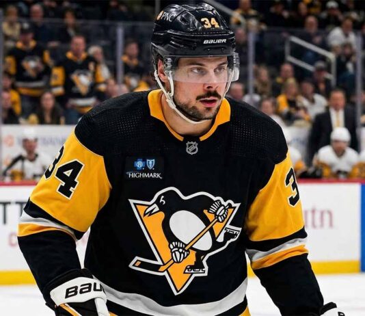 Toronto Maple Leafs captain Auston Matthews in a Pittsburgh Penguins black and gold jersey, and number 34, with a modern Highmark patch, looking towards the ice during an NHL game. Blurred arena crowd in background.