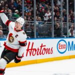 Ottawa Senators captain Brady Tkachuk skating on the ice with his stick raised during a game, amidst escalating NHL trade rumors about his future.