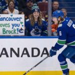 Vancouver Canucks forward Brock Boeser skating past a fan holding a handmade sign reading 'Vancouver loves you Brock!' amidst 2025-26 season trade rumors.