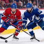 Montreal Canadiens center Nick Suzuki battles a Tampa Bay Lightning forward for puck possession during an intense NHL game.
