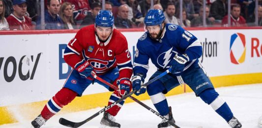 Montreal Canadiens center Nick Suzuki battles a Tampa Bay Lightning forward for puck possession during an intense NHL game.