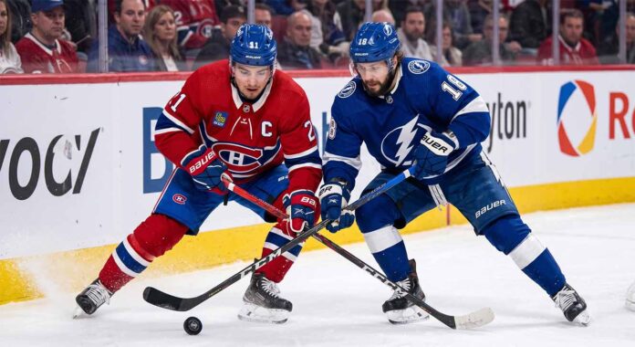 canadiens-lightning-game-3-playoffs-2026 Montreal Canadiens center Nick Suzuki battles a Tampa Bay Lightning forward for puck possession during an intense NHL game.