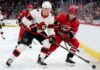 ntense action shot of an Ottawa Senators hockey player (number 7) and a Carolina Hurricanes hockey player (number 71) locked in a close puck battle on the ice during an NHL game, with other players, crowd and arena details in the background.