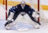 Connor Hellebuyck, star goaltender for the Winnipeg Jets, in focused butterfly stance in full navy blue and white gear in front of the net during an NHL game, amidst recent trade rumors.