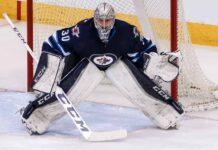 Connor Hellebuyck, star goaltender for the Winnipeg Jets, in focused butterfly stance in full navy blue and white gear in front of the net during an NHL game, amidst recent trade rumors.