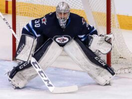 Connor Hellebuyck, star goaltender for the Winnipeg Jets, in focused butterfly stance in full navy blue and white gear in front of the net during an NHL game, amidst recent trade rumors.