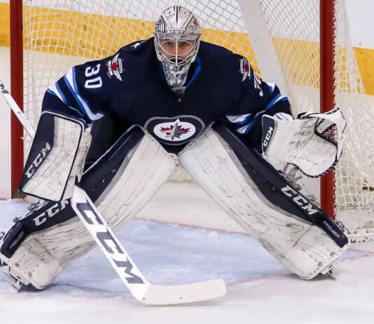 Connor Hellebuyck, star goaltender for the Winnipeg Jets, in focused butterfly stance in full navy blue and white gear in front of the net during an NHL game, amidst recent trade rumors.