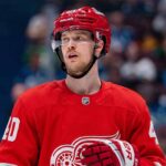 An NHL action shot featuring superstar center Elias Pettersson wearing a Detroit Red Wings home jersey, with the Red Wings' winged wheel logo.
