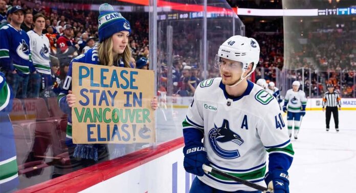 A Vancouver Canucks fan holds up a handmade sign behind the glass at Rogers Arena reading "PLEASE STAY IN VANCOUVER ELIAS!" as star center Elias Pettersson (#40) looks on from the ice during an NHL game amidst trade rumors.