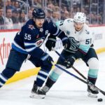 Winnipeg Jets forward Mark Scheifele (55) in navy blue jersey battles for puck possession against Seattle Kraken forward Shane Wright (51) in white away jersey during a 2025-26 NHL regular season game at Canada Life Centre.