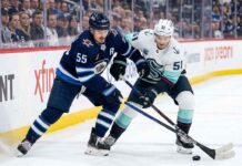 How to Watch Seattle Kraken vs. Winnipeg Jets | TV Channels & Stream Winnipeg Jets forward Mark Scheifele (55) in navy blue jersey battles for puck possession against Seattle Kraken forward Shane Wright (51) in white away jersey during a 2025-26 NHL regular season game at Canada Life Centre.