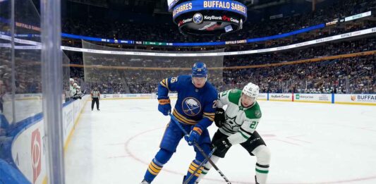 Buffalo Sabres defenseman Rasmus Dahlin (26) in blue battles Dallas Stars forward Jason Robertson (21) in white for the puck during an NHL game at KeyBank Center.