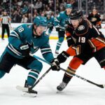 Cutter Gauthier of the Anaheim Ducks, wearing jersey #19, and Macklin Celebrini of the San Jose Sharks, wearing jersey #18, in a face-off battle for the puck on the ice at Honda Center. The arena has Honda Center and Victory+ signage in the background during a San Jose Sharks vs Anaheim Ducks game.
