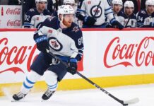 Kyle Connor #81 of the Winnipeg Jets skating with the puck, subject of significant NHL offseason trade rumors, against boards with Coca-Cola logos.
