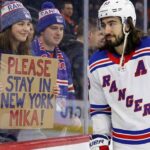 New York Rangers center Mika Zibanejad skates near a fan holding a hand-written sign that reads 'PLEASE STAY IN NEW YORK MIKA!', visually reinforcing his connection to the fans and silencing recent NHL trade rumors.