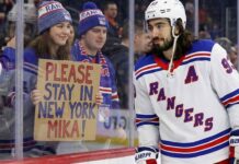 New York Rangers center Mika Zibanejad skates near a fan holding a hand-written sign that reads 'PLEASE STAY IN NEW YORK MIKA!', visually reinforcing his connection to the fans and silencing recent NHL trade rumors.