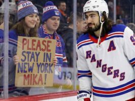 New York Rangers center Mika Zibanejad skates near a fan holding a hand-written sign that reads 'PLEASE STAY IN NEW YORK MIKA!', visually reinforcing his connection to the fans and silencing recent NHL trade rumors.