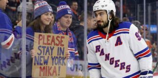 New York Rangers center Mika Zibanejad skates near a fan holding a hand-written sign that reads 'PLEASE STAY IN NEW YORK MIKA!', visually reinforcing his connection to the fans and silencing recent NHL trade rumors.