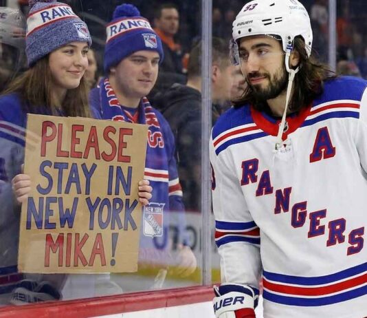 New York Rangers center Mika Zibanejad skates near a fan holding a hand-written sign that reads 'PLEASE STAY IN NEW YORK MIKA!', visually reinforcing his connection to the fans and silencing recent NHL trade rumors.