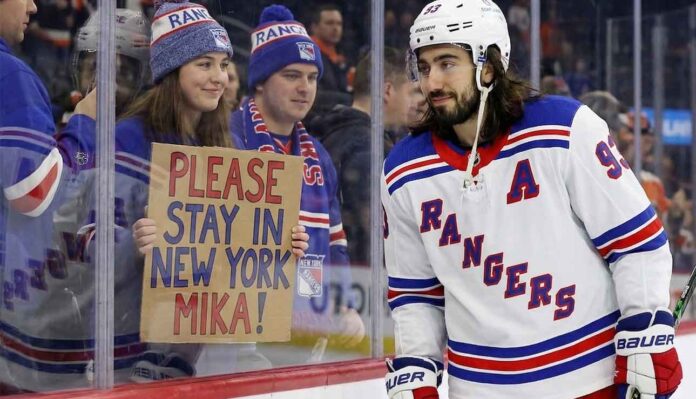 New York Rangers center Mika Zibanejad skates near a fan holding a hand-written sign that reads 'PLEASE STAY IN NEW YORK MIKA!', visually reinforcing his connection to the fans and silencing recent NHL trade rumors.