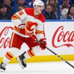 CALGARY FLAMES CENTER MORGAN FROST (16) SKATING DOWN THE ICE IN A WHITE AWAY JERSEY DURING AN NHL GAME, AMID TRADE RUMORS.