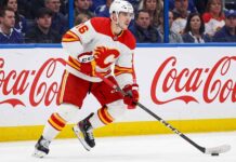 CALGARY FLAMES CENTER MORGAN FROST (16) SKATING DOWN THE ICE IN A WHITE AWAY JERSEY DURING AN NHL GAME, AMID TRADE RUMORS.