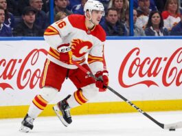 CALGARY FLAMES CENTER MORGAN FROST (16) SKATING DOWN THE ICE IN A WHITE AWAY JERSEY DURING AN NHL GAME, AMID TRADE RUMORS.