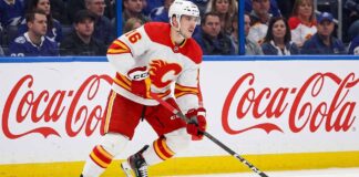 CALGARY FLAMES CENTER MORGAN FROST (16) SKATING DOWN THE ICE IN A WHITE AWAY JERSEY DURING AN NHL GAME, AMID TRADE RUMORS.