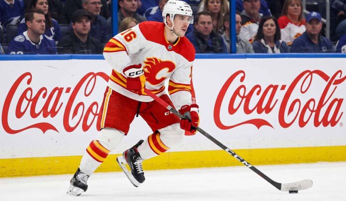 CALGARY FLAMES CENTER MORGAN FROST (16) SKATING DOWN THE ICE IN A WHITE AWAY JERSEY DURING AN NHL GAME, AMID TRADE RUMORS.