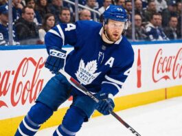 Morgan Rielly Trade Rumors: Will He Leave the Toronto Maple Leafs? Toronto Maple Leafs defenseman Morgan Rielly #44 skating in an NHL game, holding a hockey stick near the Coca-Cola branded boards.