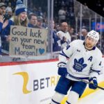 Toronto Maple Leafs defenseman Morgan Rielly skates past a young fan holding a cardboard sign that reads "Good luck on your new team Morgan!" amid persistent trade rumors.