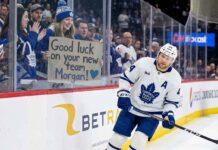 Toronto Maple Leafs defenseman Morgan Rielly skates past a young fan holding a cardboard sign that reads "Good luck on your new team Morgan!" amid persistent trade rumors.