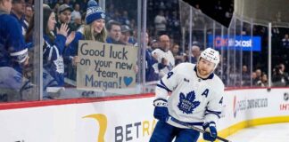 Toronto Maple Leafs defenseman Morgan Rielly skates past a young fan holding a cardboard sign that reads "Good luck on your new team Morgan!" amid persistent trade rumors.