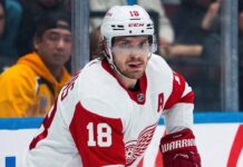 St. Louis Blues center Robert Thomas (wearing jersey number 18 and a white helmet with a clear visor) looking intense during an NHL game. He is a reported blockbuster trade target for the Detroit Red Wings to fix their 5v5 scoring and end their playoff drought.