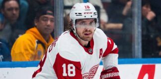 St. Louis Blues center Robert Thomas (wearing jersey number 18 and a white helmet with a clear visor) looking intense during an NHL game. He is a reported blockbuster trade target for the Detroit Red Wings to fix their 5v5 scoring and end their playoff drought.