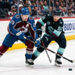 Nathan MacKinnon and Shane Wright clashing sticks during a puck battle at Ball Arena.