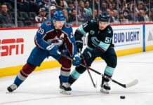 Nathan MacKinnon and Shane Wright clashing sticks during a puck battle at Ball Arena.