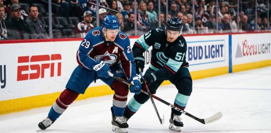 Nathan MacKinnon and Shane Wright clashing sticks during a puck battle at Ball Arena.