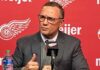 Detroit Red Wings GM Steve Yzerman making distinct hand gestures while speaking intensely at a press conference microphone amidst rumors about his future.