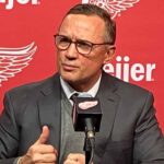 Detroit Red Wings GM Steve Yzerman making distinct hand gestures while speaking intensely at a press conference microphone amidst rumors about his future.