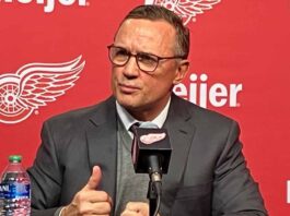 Detroit Red Wings GM Steve Yzerman making distinct hand gestures while speaking intensely at a press conference microphone amidst rumors about his future.