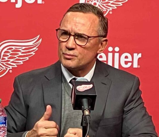 Detroit Red Wings GM Steve Yzerman making distinct hand gestures while speaking intensely at a press conference microphone amidst rumors about his future.