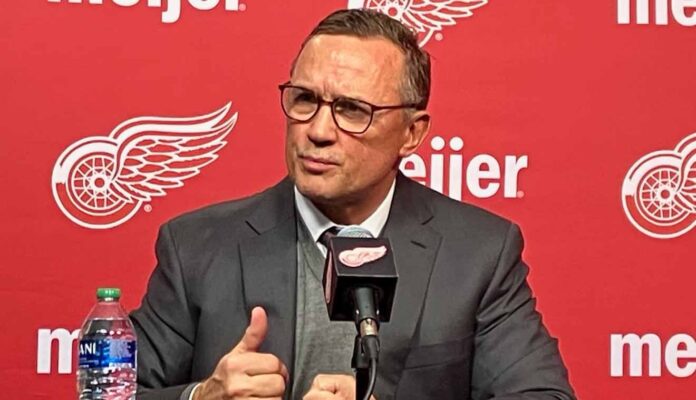 Detroit Red Wings GM Steve Yzerman making distinct hand gestures while speaking intensely at a press conference microphone amidst rumors about his future.