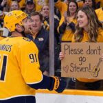 Steven Stamkos of the Nashville Predators in a yellow jersey looks at a female fan holding a cardboard sign that says 'Please don't go Steven!' amidst offseason trade rumors.