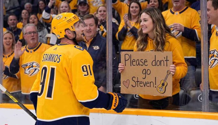 Steven Stamkos of the Nashville Predators in a yellow jersey looks at a female fan holding a cardboard sign that says 'Please don't go Steven!' amidst offseason trade rumors.