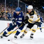 Tampa Bay Lightning's Nikita Kucherov (86) and Boston Bruins' David Pastrnak (88) battle for puck possession along the boards during an intense Atlantic Division NHL game.