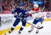 Dynamic on-ice action photo from Game 4 of the 2026 Stanley Cup Playoffs, showing Tampa Bay Lightning forward Nikita Kucherov (#86, blue jersey) battling Montreal Canadiens defenseman Lane Hutson (#?, white jersey) for puck possession near the boards in a packed Bell Centre.