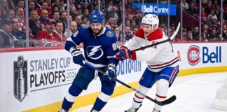 Dynamic on-ice action photo from Game 4 of the 2026 Stanley Cup Playoffs, showing Tampa Bay Lightning forward Nikita Kucherov (#86, blue jersey) battling Montreal Canadiens defenseman Lane Hutson (#?, white jersey) for puck possession near the boards in a packed Bell Centre.